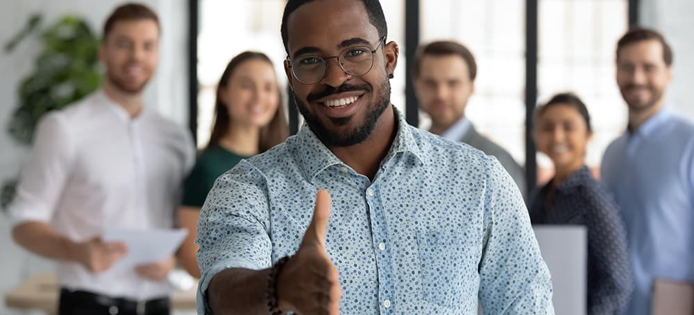 Homme noir au travail souriant avec main tendue et son équipe derrière lui