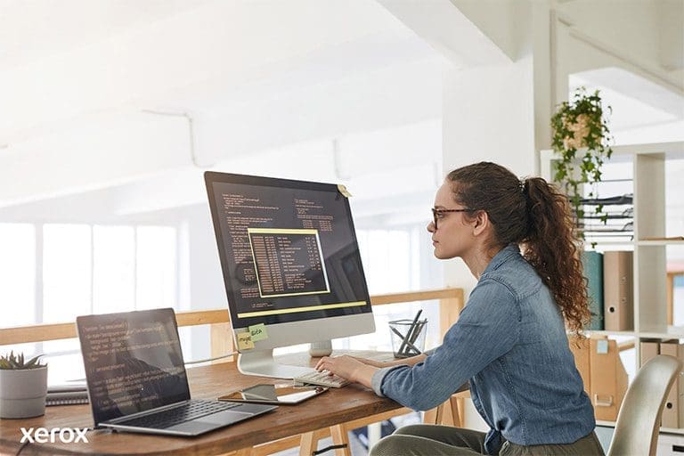 Une femme à son bureau, occupée avec un ordinateur et un ordinateur portable, démontrant sa productivité dans un espace de travail moderne. Une femme à son bureau, occupée avec un ordinateur et un ordinateur portable, démontrant sa productivité dans un espace de travail moderne.