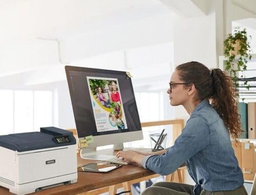 Une femme assise à un bureau, concentrée sur son travail, avec une imprimante Xerox® C320 couleur