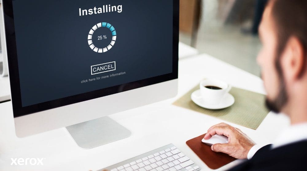 Xerox® Smart Start : Installation simple et rapide Vue rapprochée d'un écran d'ordinateur affichant une barre de progression « Installation » à 25 %, avec la main d'une personne sur une souris d'ordinateur à côté d'une tasse à café, illustrant une configuration logicielle facile.